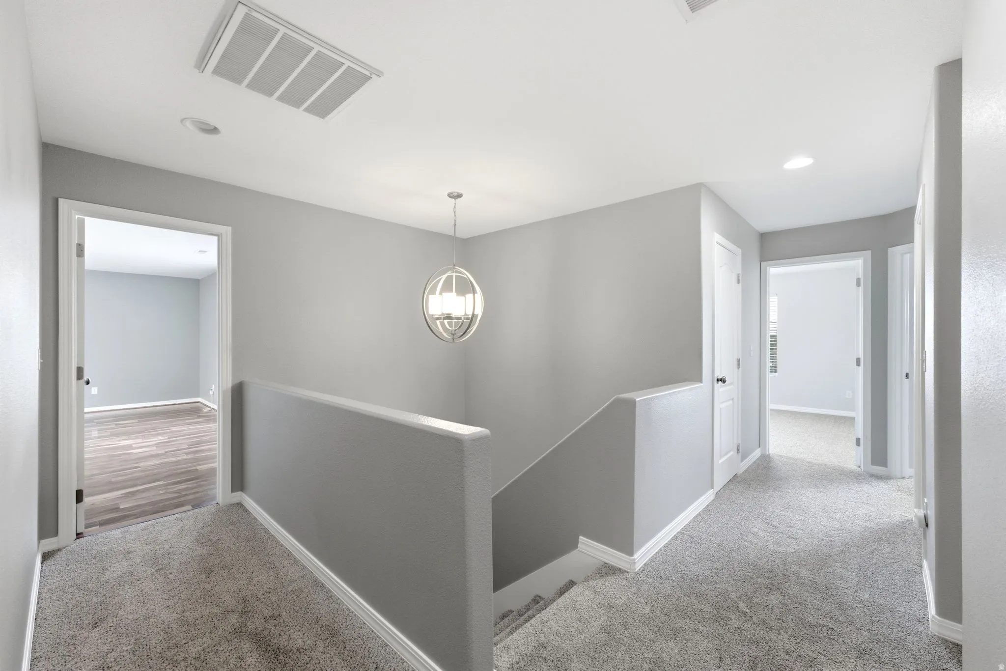 Upper-level landing featuring light gray carpeting and walls, a modern spherical pendant light, and white trim