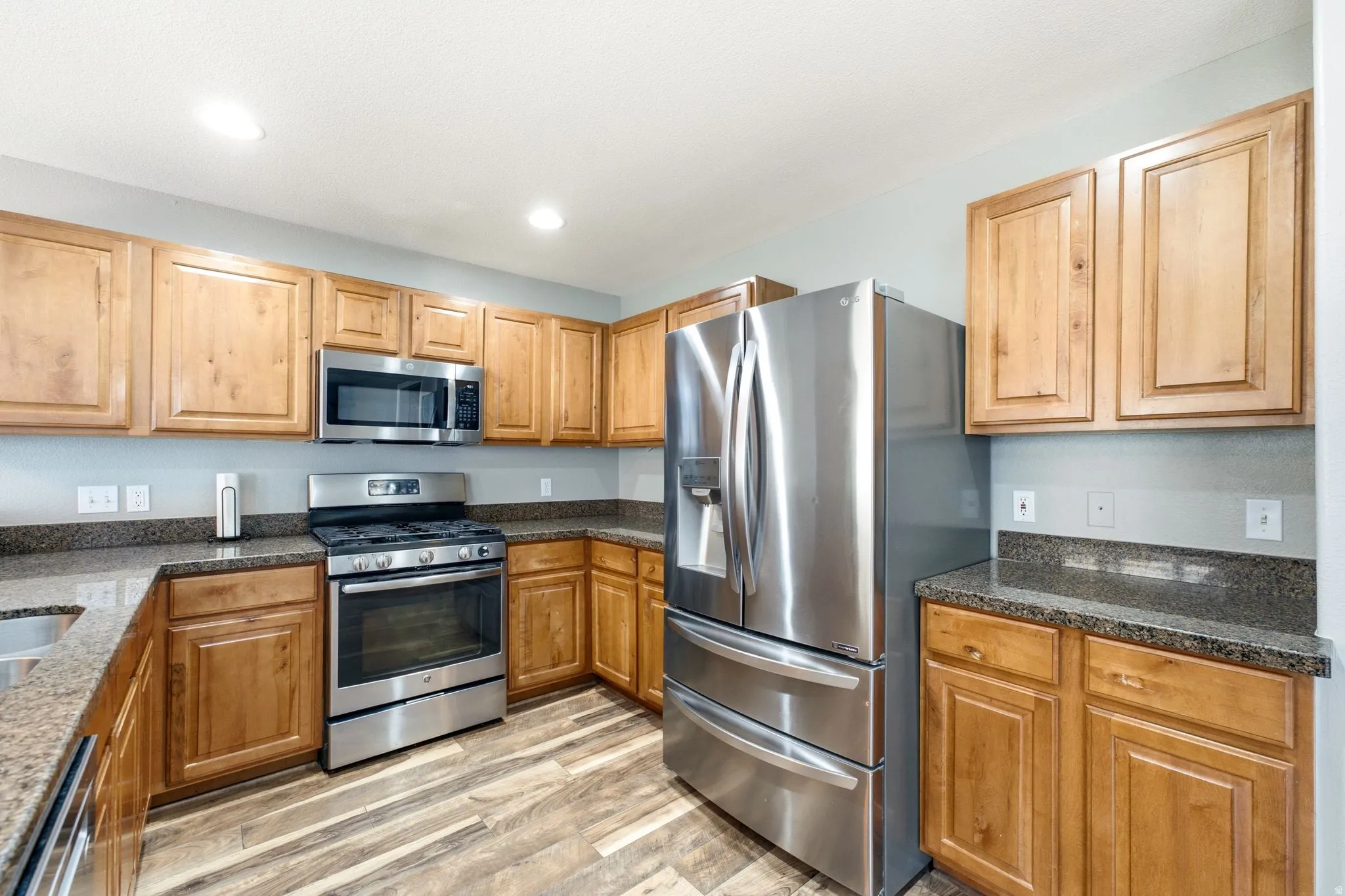 Kitchen featuring wood cabinetry, stainless steel appliances, granite-finish countertops, and wood-finish flooring