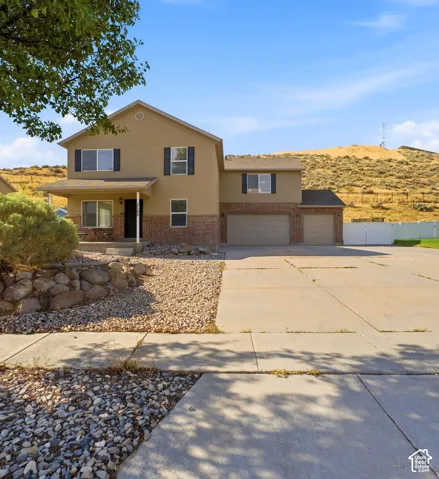 Two-story exterior with stucco and brick facade, covered front porch, dual garages, and a gravel front yard
