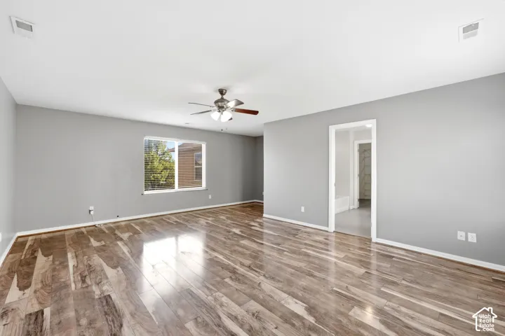 Spacious room featuring wood-finish flooring, a window with horizontal blinds, a ceiling fan, and light gray wall finishes