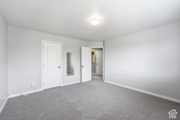 Carpeted room featuring light gray wall paint, a flush-mount ceiling light fixture, white baseboards, and white interior doors with black hardware