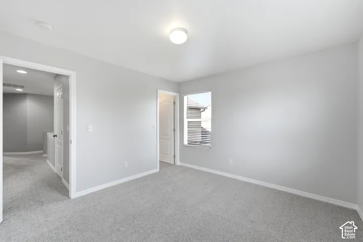 Spacious room featuring light gray carpeting, neutral wall paint, white trim, and a window with blinds