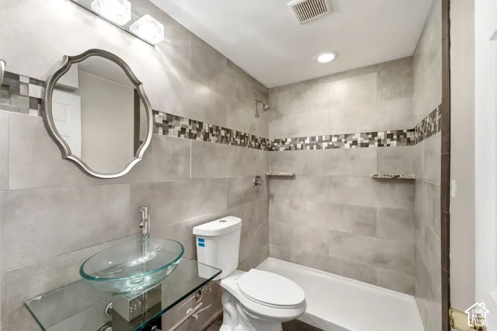 Bathroom featuring full-height tiled walls, a decorative mosaic tile band, and a glass vessel sink set on a glass vanity