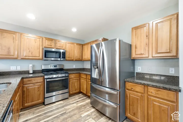Kitchen featuring wood cabinetry, stainless steel appliances, granite-finish countertops, and wood-finish flooring