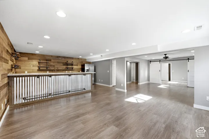 Open-concept room featuring wood-finish flooring, a corrugated metal and wood-paneled bar with a light-colored countertop, recessed lighting, and white barn doors