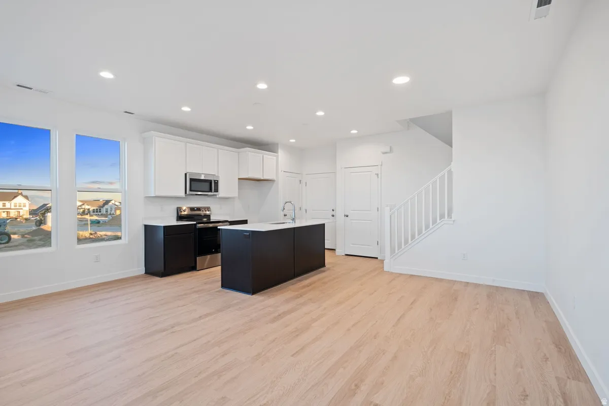 Open concept living area featuring light wood-finish flooring, recessed lighting, and bright white walls