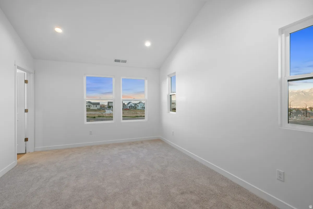 Spacious room featuring vaulted ceilings, recessed lighting, neutral carpet flooring, and multiple windows providing ample natural light