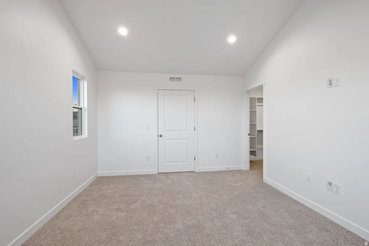Carpeted room featuring recessed lighting, a single window, a standard door, and an open doorway revealing built-in shelving
