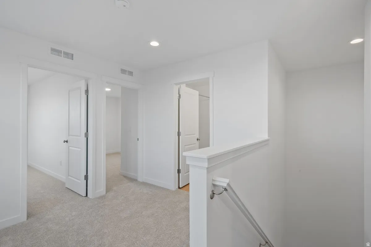 Upper-level landing featuring light-toned carpeting, white walls, recessed lighting, and white paneled doors with black hardware
