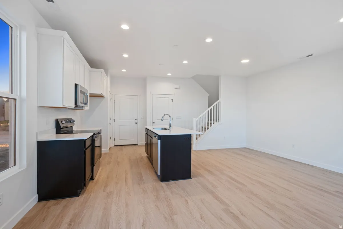 Modern kitchen featuring white upper cabinetry, black lower cabinetry, and a central island with a sink