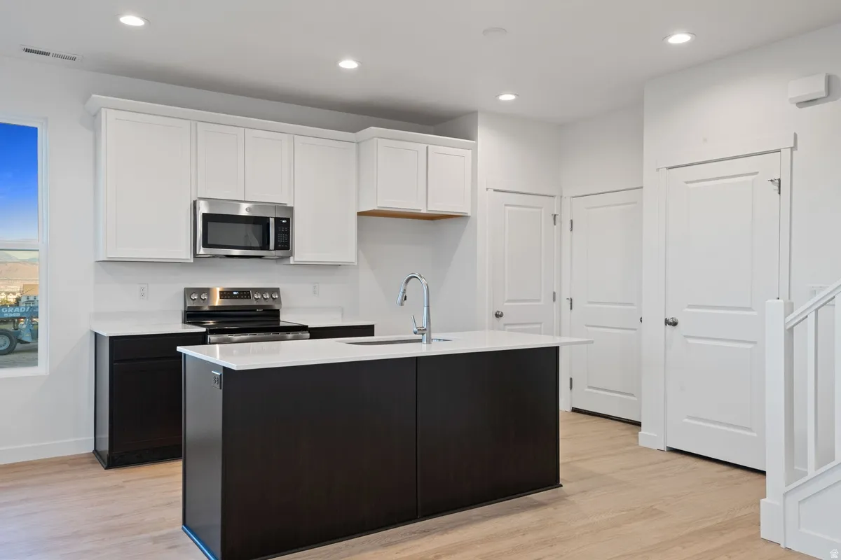 Modern kitchen featuring a two-tone cabinetry design with white upper cabinets and dark lower cabinets, stainless steel appliances, a center island with a sink, white countertops, and recessed lighting