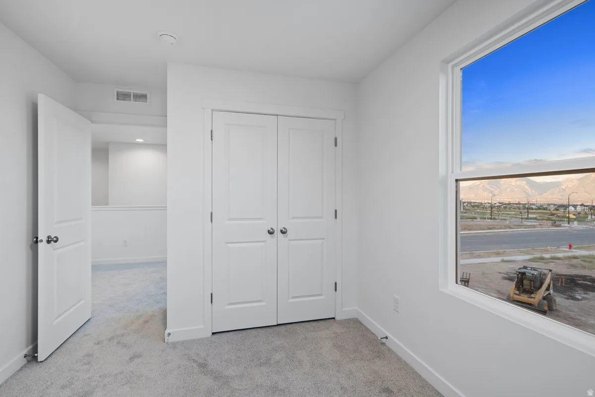 Neutral tone paint throughout, featuring a double-door closet, a large window, and light gray carpeting
