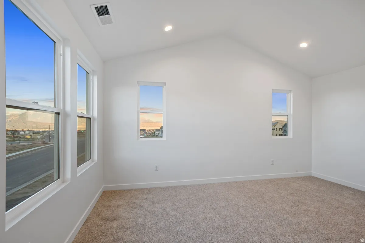 Carpeted room featuring multiple windows, a vaulted ceiling, recessed lighting, and a neutral color palette