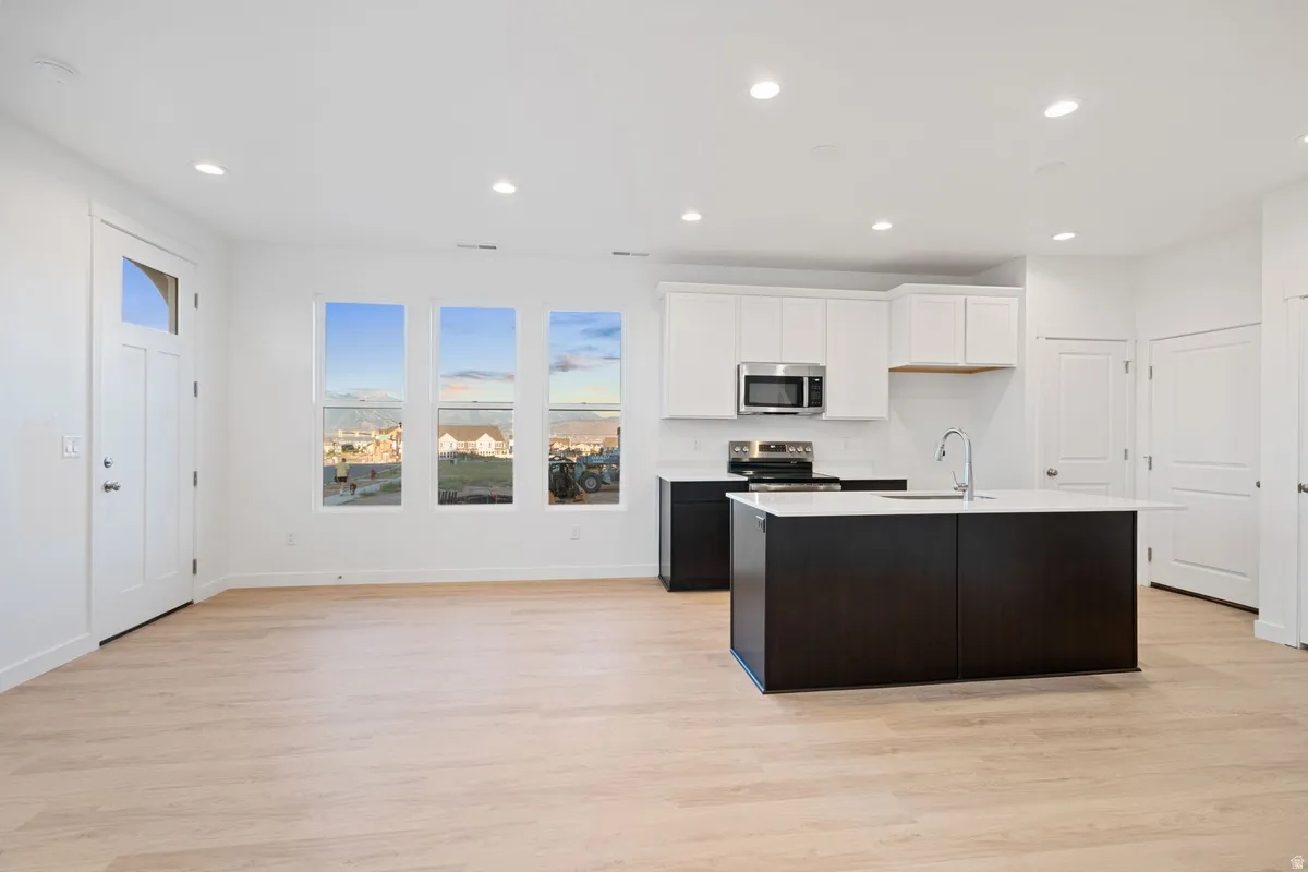 Open-concept living space featuring wood-finish flooring, recessed lighting, and a white kitchen with a dark-toned island