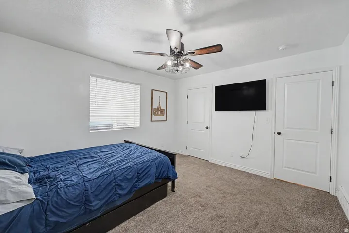 Carpeted room featuring a ceiling fan with light fixture, window with horizontal blinds, and two panel doors