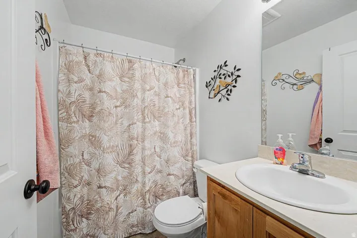 Bathroom featuring a shower with a shower curtain, a toilet, a vanity with a laminate countertop, and a built-in mirror