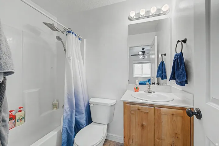 Bathroom featuring a shower/tub combination with a wall-mounted showerhead, a single vanity with a laminate countertop, and a wood-finish cabinet
