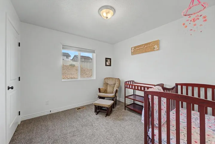 Carpeted room featuring a white door with black hardware, a window with exterior residential structures, white baseboards, and a flush-mount ceiling light fixture