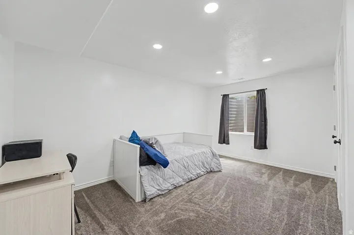 Room featuring recessed lighting, a window with horizontal blinds and dark drapery, light gray wall-to-wall carpeting, and white painted walls