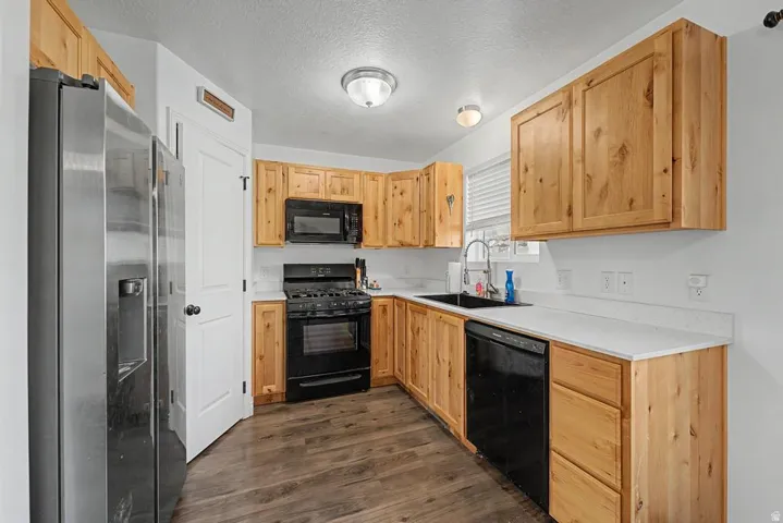 Kitchen featuring natural wood cabinetry, a stainless steel refrigerator, black gas range, built-in microwave, and a black sink with a chrome faucet