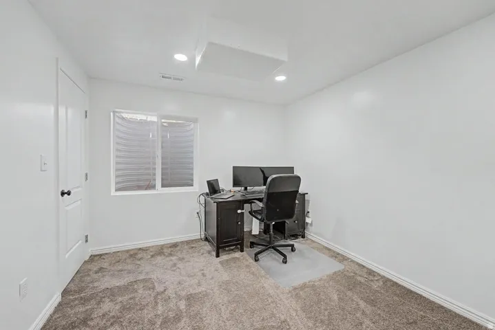 Room featuring neutral carpeting, a white painted door with black hardware, and an egress window with blinds