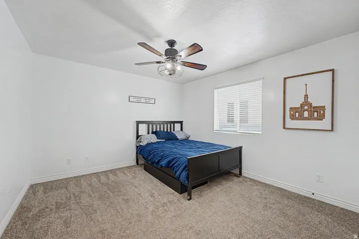 Bedroom featuring neutral wall paint, gray carpet flooring, a ceiling fan with integrated lighting, and a single window with blinds
