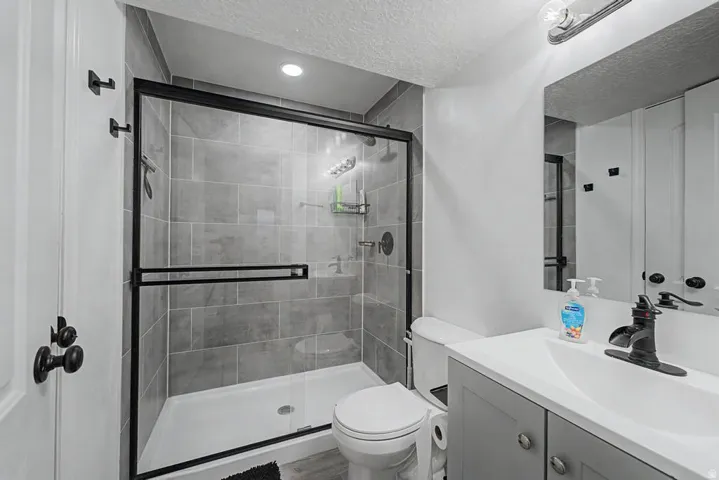 Bathroom featuring a glass-enclosed shower with gray tiled walls, a white shower base, and a matte black shower fixture