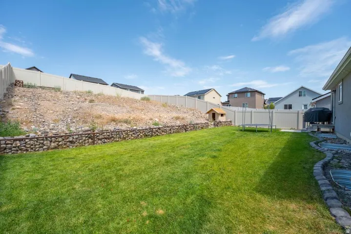 Expansive backyard featuring a lush lawn, a gabion retaining wall, and a full perimeter fence