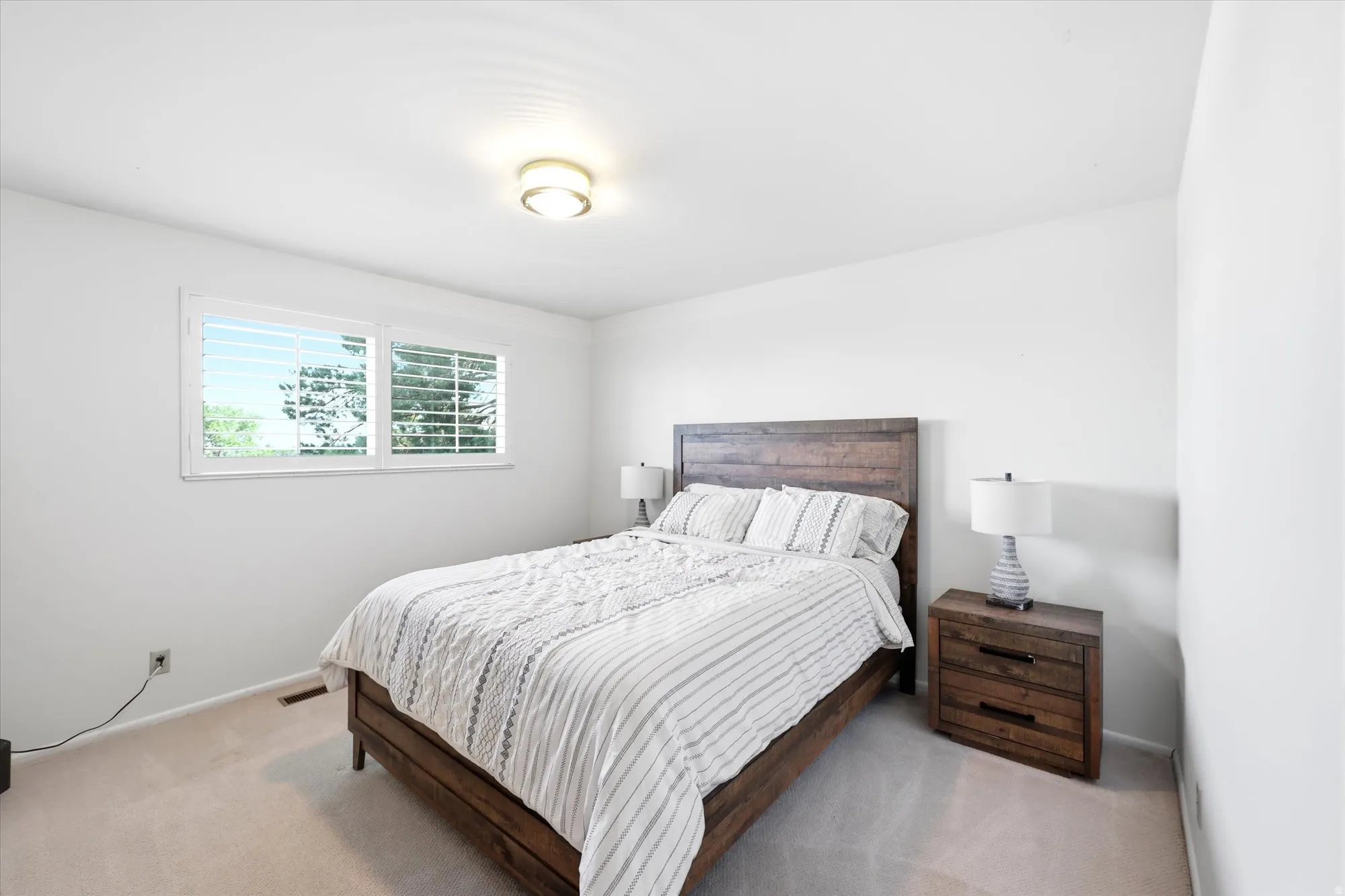 Bedroom featuring a double window with plantation shutters, light-colored carpeting, a contemporary ceiling light fixture, and white painted walls