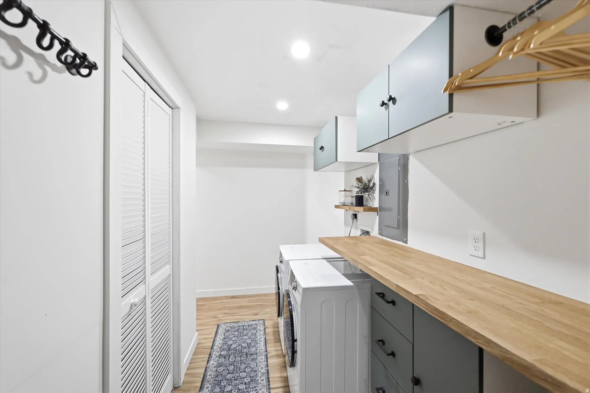 Laundry area featuring a wood-finish countertop, white cabinetry with black hardware, and louvered bi-fold doors