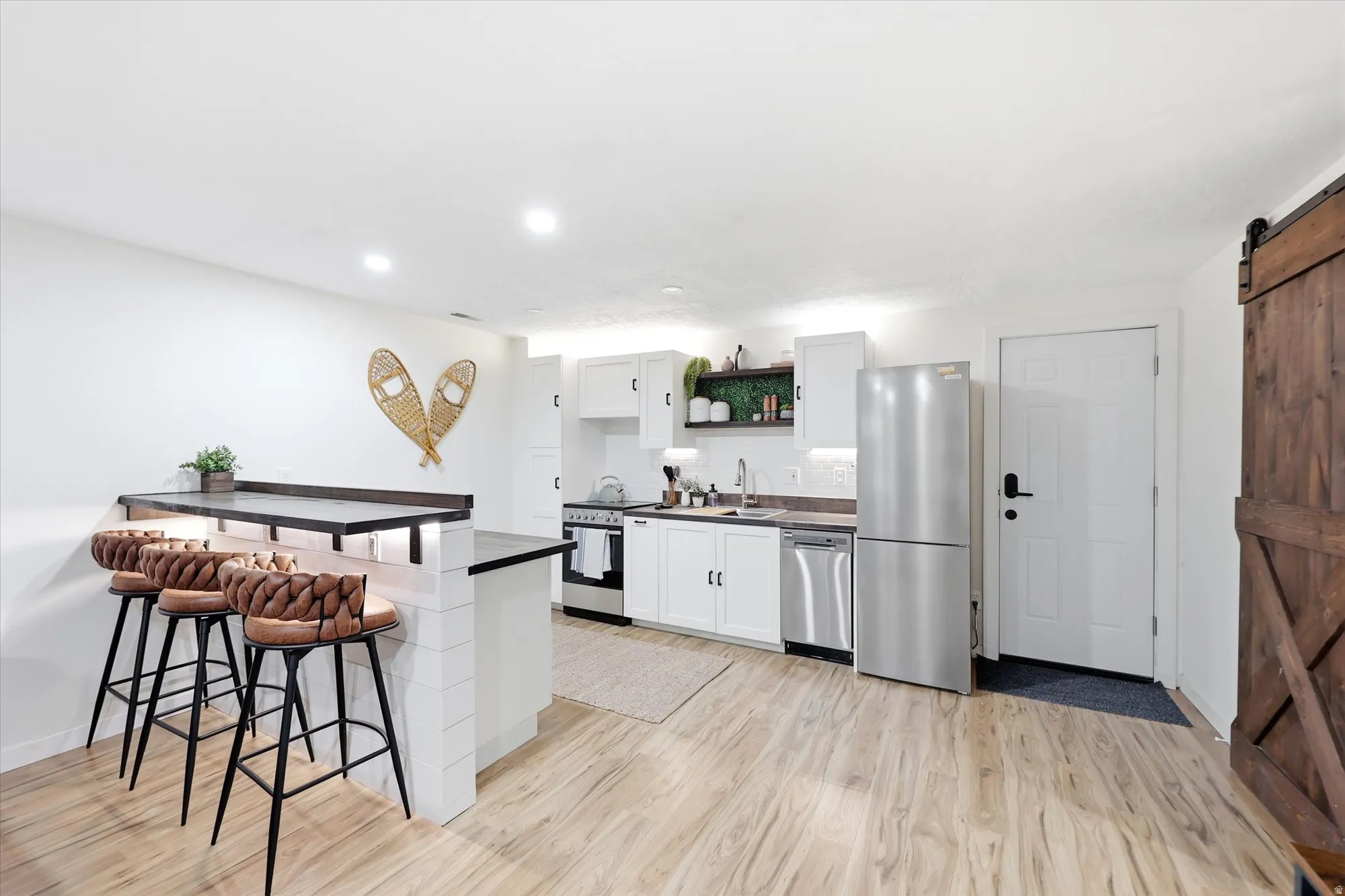 Open-concept kitchen featuring white cabinetry, stainless steel appliances, and a breakfast bar with dark countertops