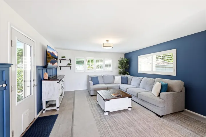 Spacious living area featuring a prominent accent wall, multiple windows with white plantation shutters, and light wood-finish flooring