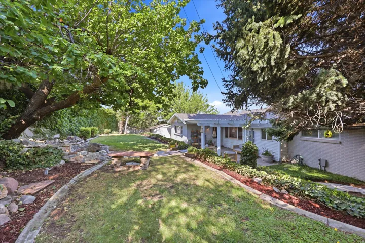 Expansive backyard featuring a manicured lawn, established shade trees, a multi-tiered rock garden, and a stone bench