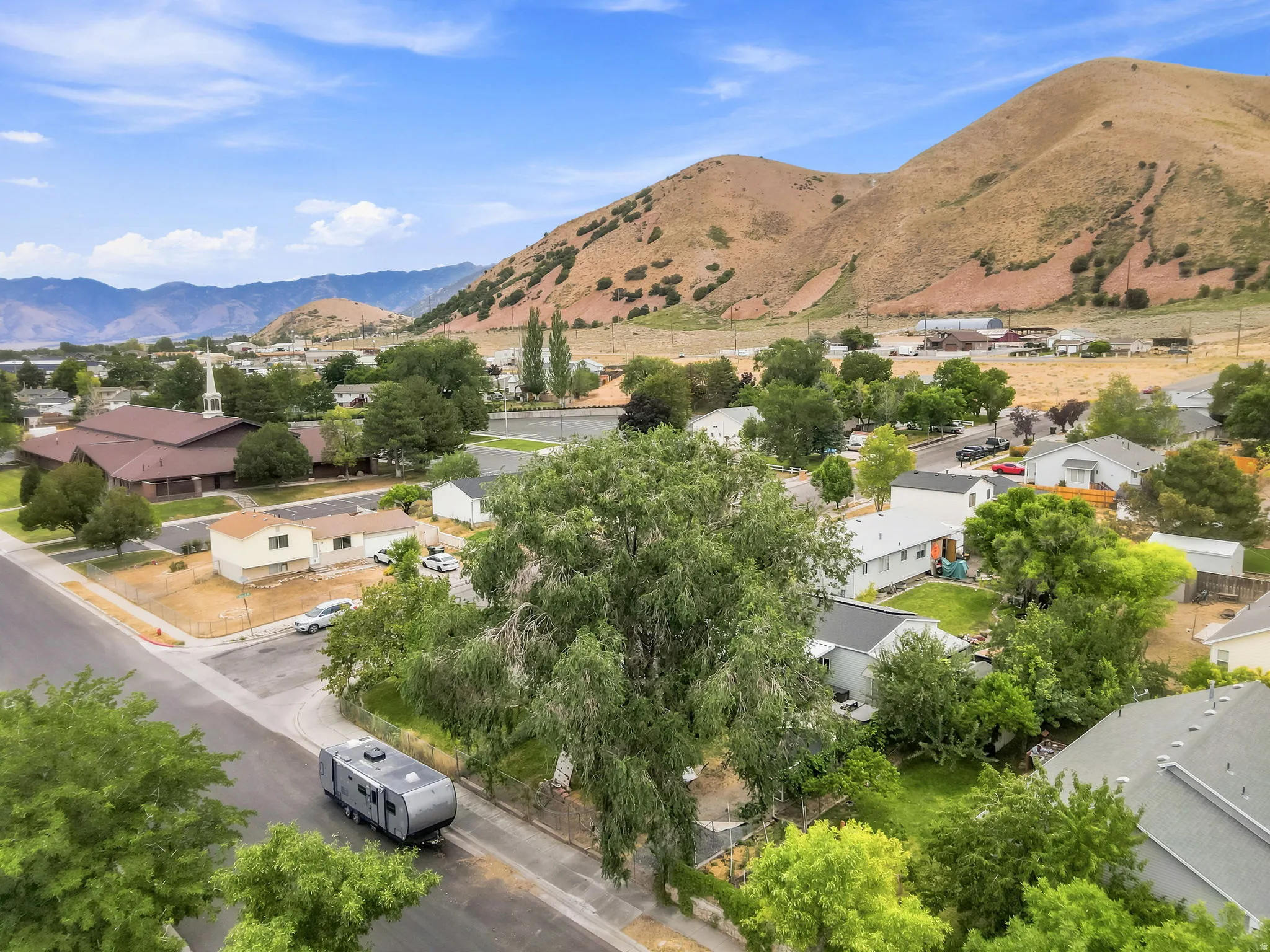 Residential neighborhood with established trees, set against a backdrop of natural hills and distant mountains