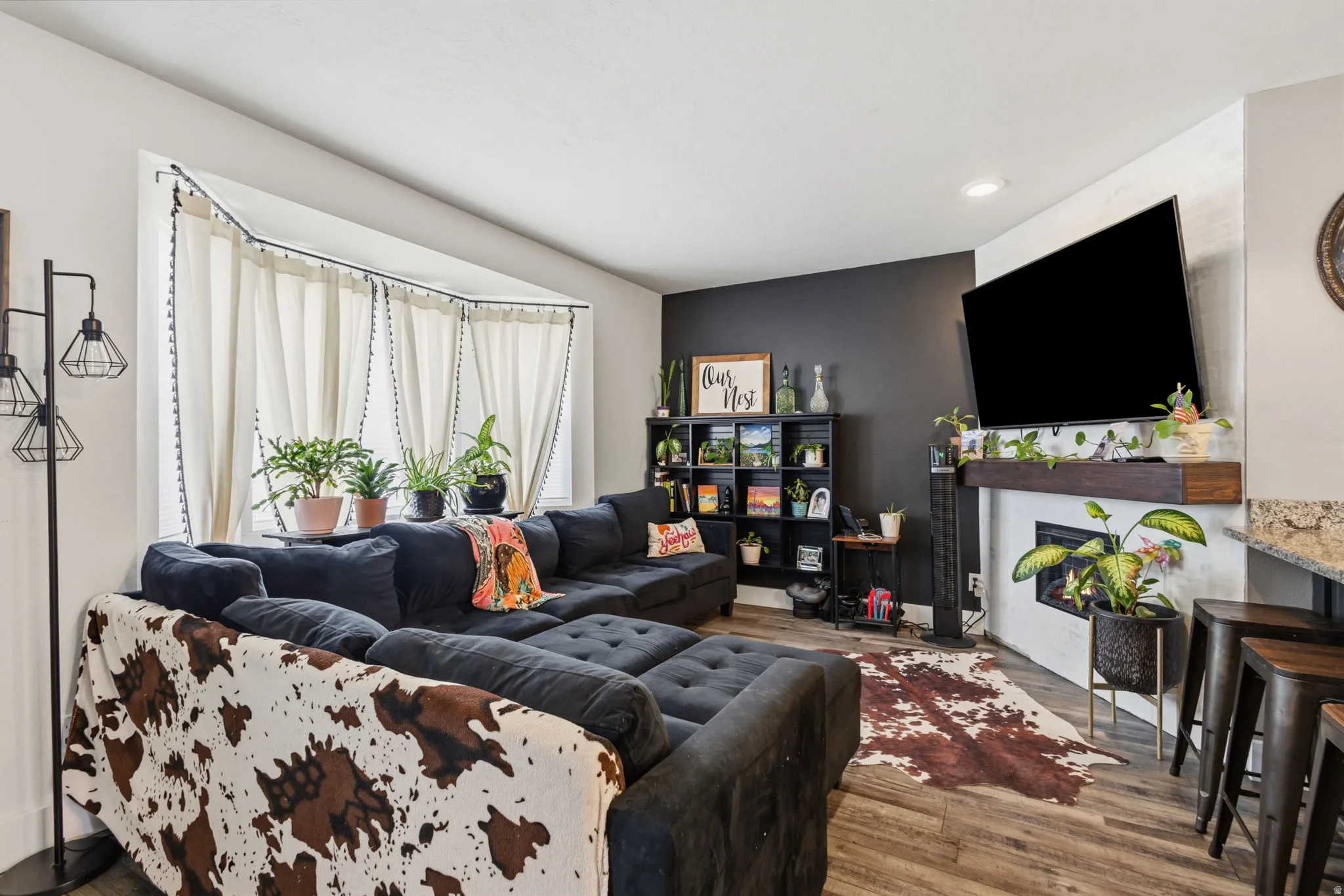 Living area featuring wood-finish flooring, a contemporary fireplace with a wood mantle, and a bay window with natural light