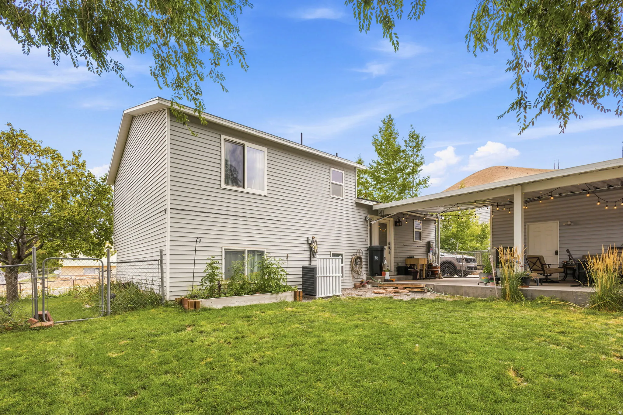 Expansive backyard featuring a manicured lawn, chain-link fencing, and a concrete patio with a covered outdoor area