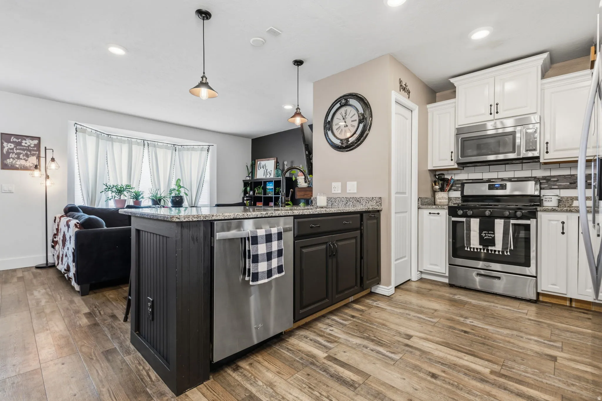 Kitchen featuring stainless steel appliances, wood-finish flooring, white upper cabinetry, dark lower cabinetry, and a central island with a granite-style countertop