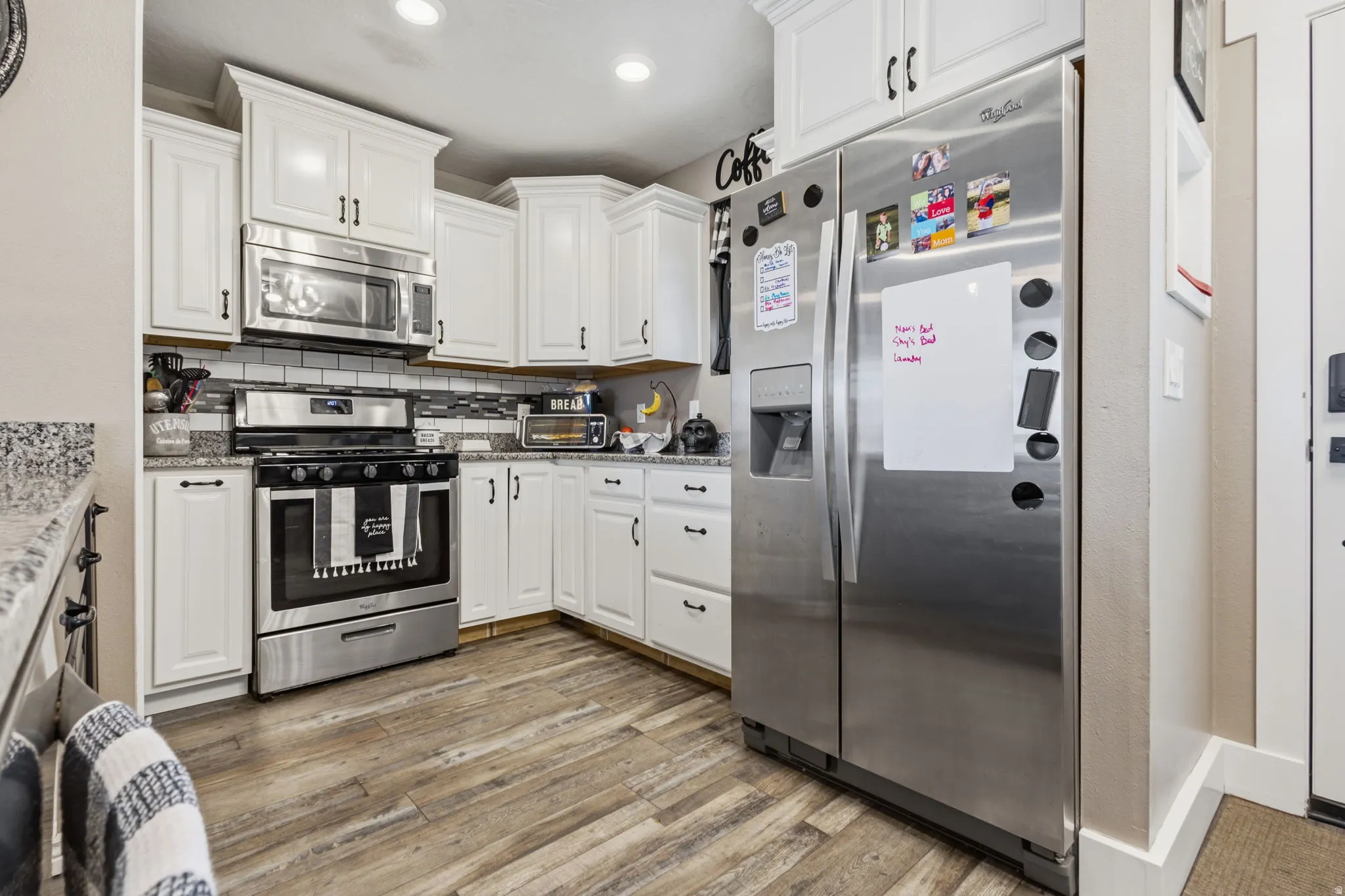 Kitchen featuring white cabinetry, stainless steel appliances, wood-finish flooring, granite countertops, and a tile backsplash