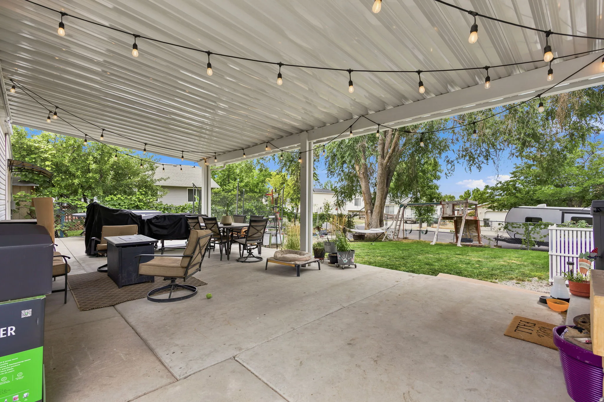 Expansive covered patio featuring a corrugated metal roof, string lighting, and a concrete slab