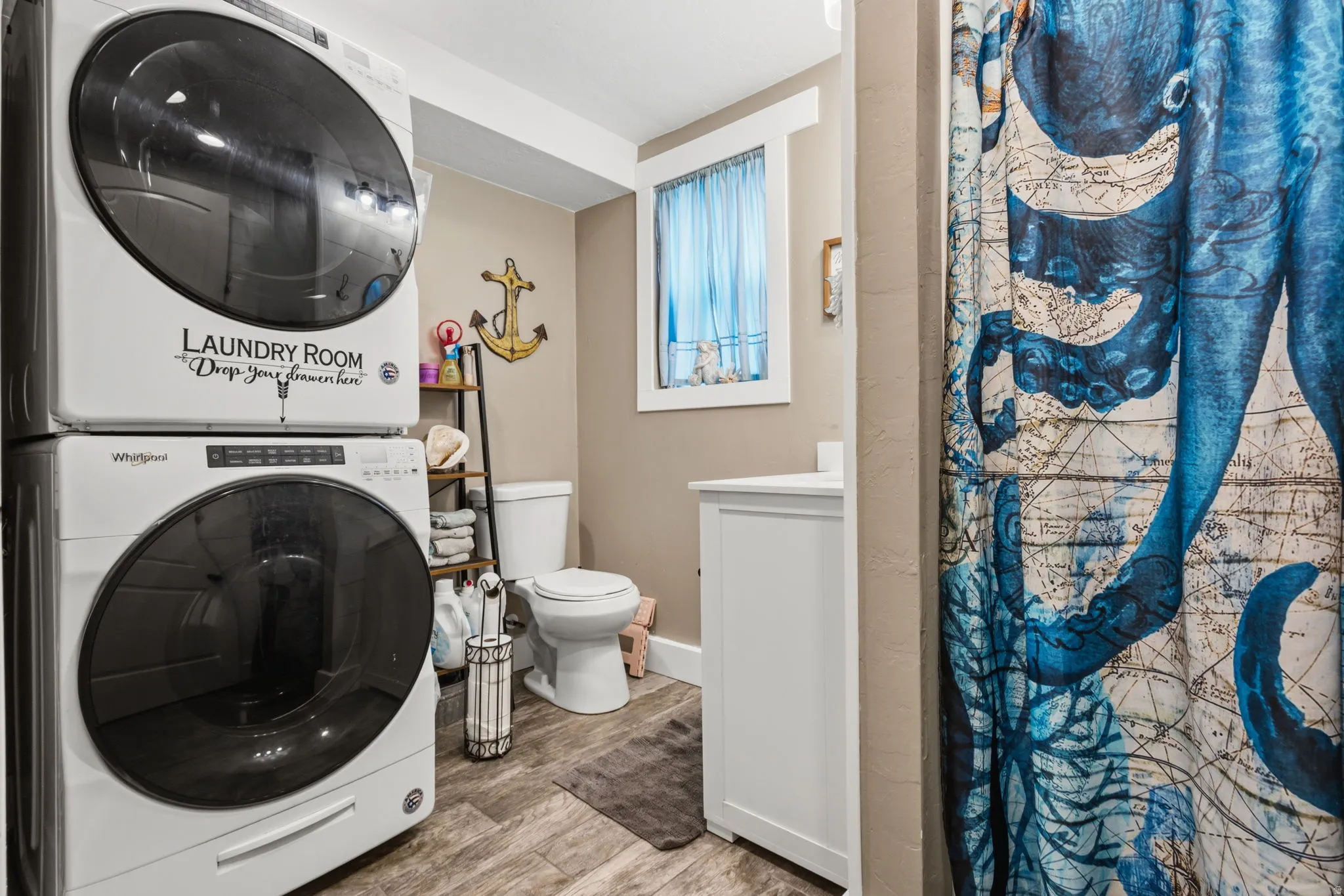 Laundry area featuring stacked front-load washer and dryer, wood-finish flooring, and a window with white trim