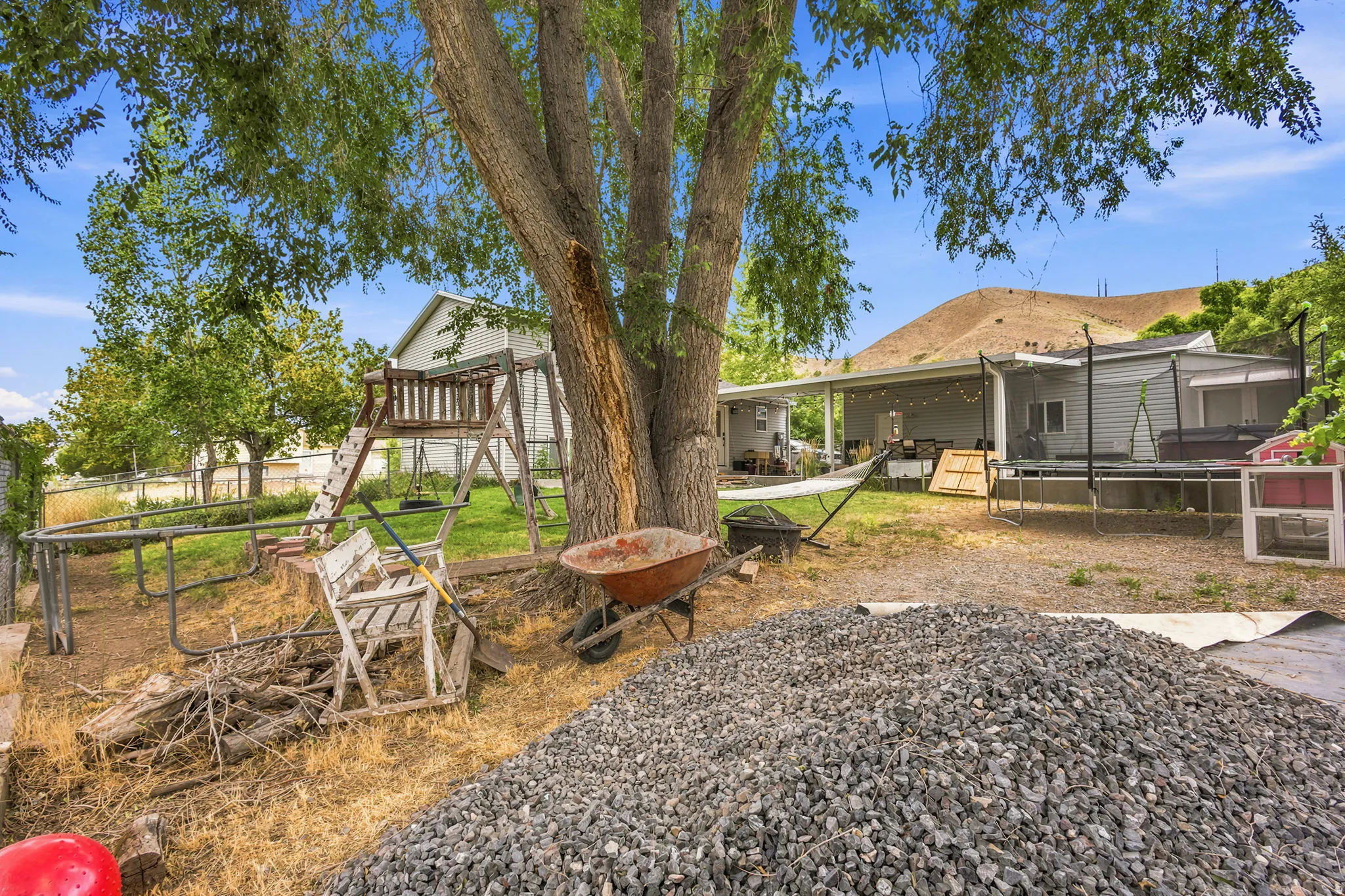 Expansive backyard featuring a mature tree, a covered patio, and a backdrop of natural terrain