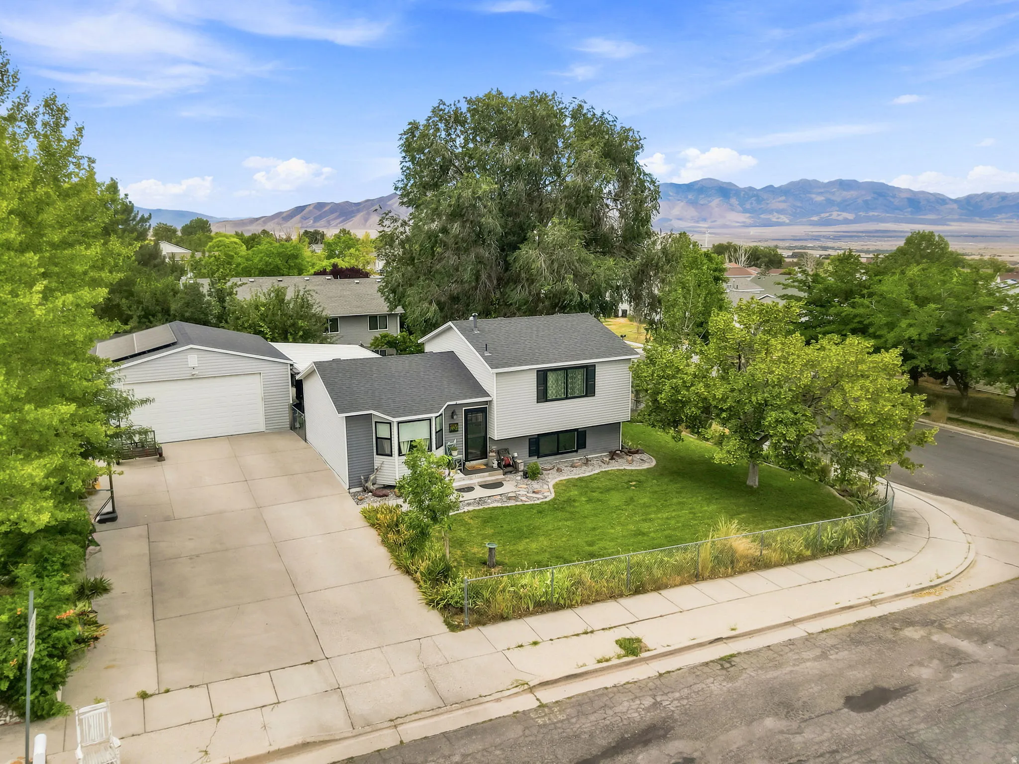 Split-level residence featuring a two-car garage, expansive concrete driveway, and front lawn with mature trees