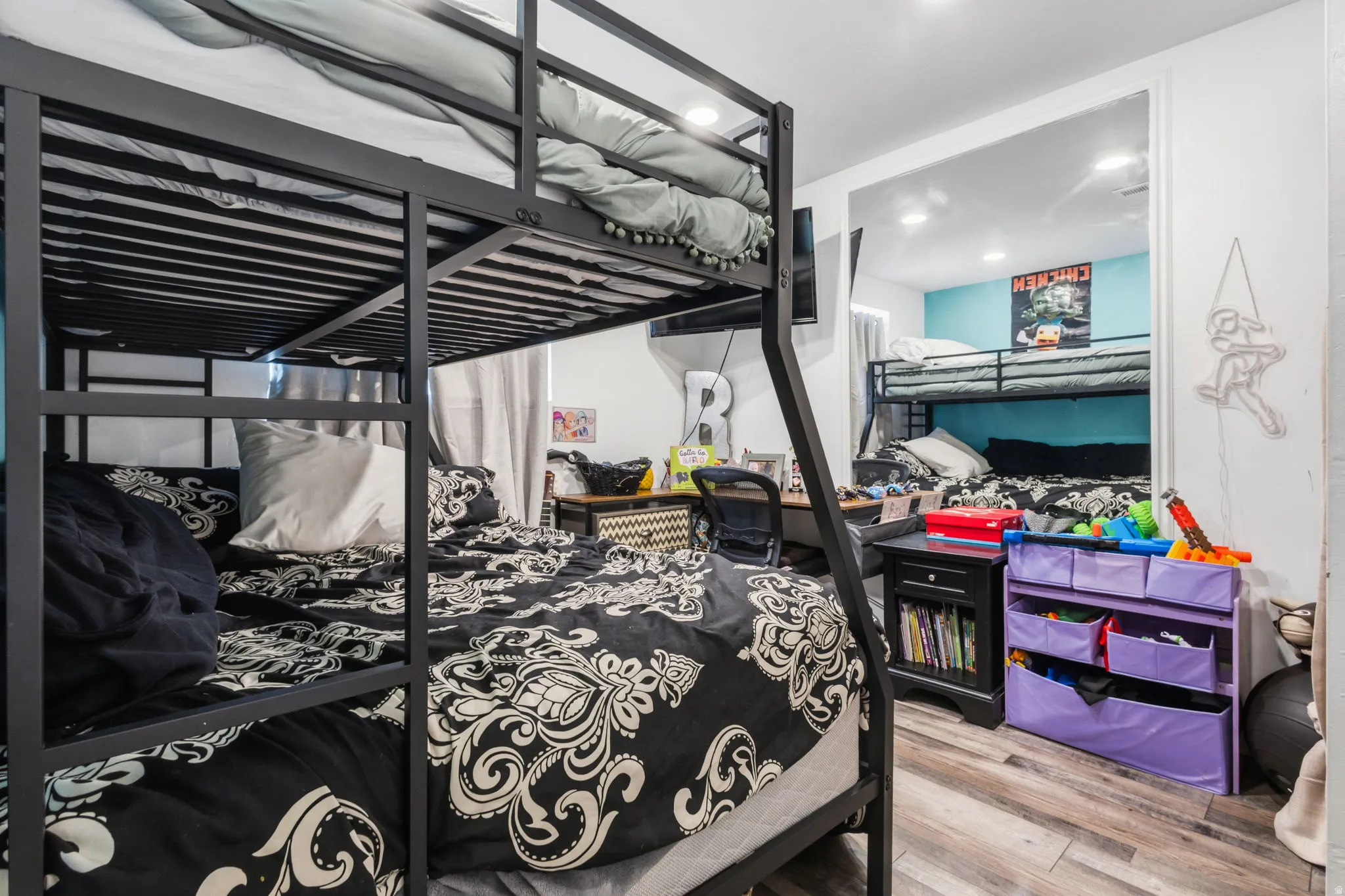 Room featuring two sets of black metal bunk beds, light wood-finish flooring, and white walls with a partial accent wall in light blue