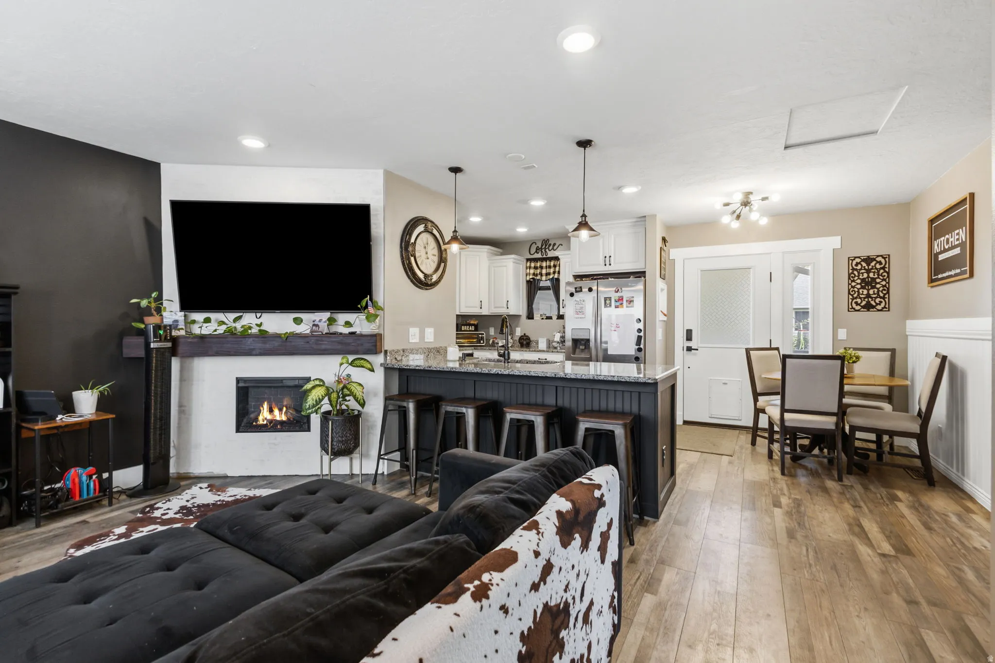Open-concept living space featuring wood-finish flooring, a white-painted fireplace surround with a dark wood mantel, and recessed lighting