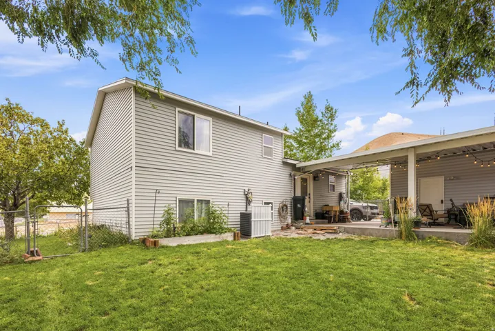 Expansive backyard featuring a manicured lawn, chain-link fencing, and a concrete patio with a covered outdoor area