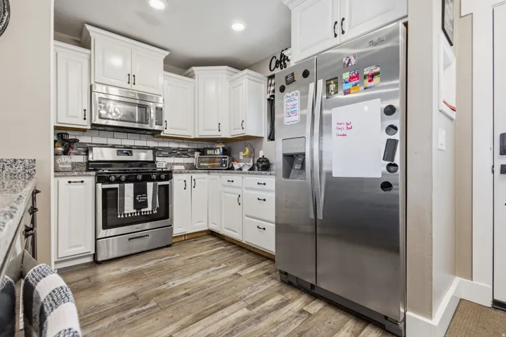 Kitchen featuring white cabinetry, stainless steel appliances, wood-finish flooring, granite countertops, and a tile backsplash