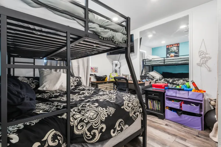 Room featuring two sets of black metal bunk beds, light wood-finish flooring, and white walls with a partial accent wall in light blue