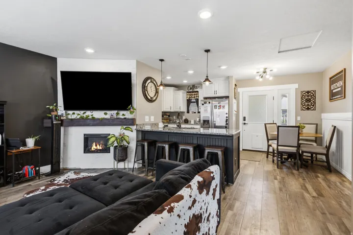 Open-concept living space featuring wood-finish flooring, a white-painted fireplace surround with a dark wood mantel, and recessed lighting
