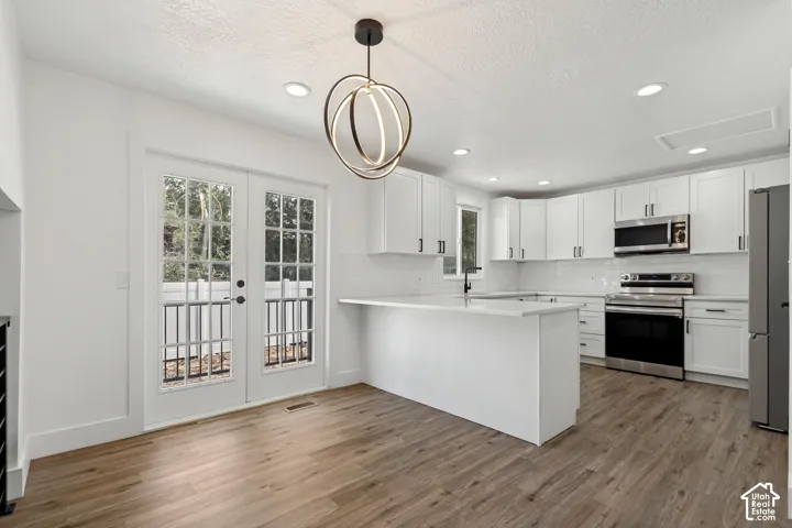 Open-concept kitchen featuring white cabinetry, stainless steel appliances, a central island with countertop seating, and wood-finish flooring