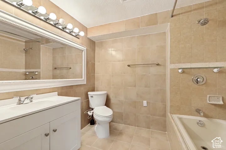 Bathroom featuring floor-to-ceiling tile, a single vanity with storage, a large framed mirror, a six-bulb vanity light, and a combined tub and shower
